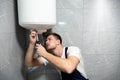 Young handsome smiling man worker in uniform with screwdriver in his hand repairing boiler at home in the toilette professional