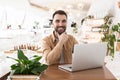 Young handsome smiling man works in his laptop during lunch break at cafe holding his hands near chin looking happy, multitasking Royalty Free Stock Photo