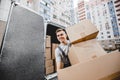 A young handsome smiling worker wearing uniform is unloading the van full of boxes. The block of flats is in the Royalty Free Stock Photo