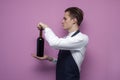 Young handsome sommelier opens a bottle of wine on a colored background, the guy the waiter holds red wine Royalty Free Stock Photo