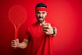 Young handsome sportsman with beard playing tennis using racket over red background annoyed and frustrated shouting with anger,