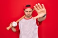 Young handsome sporty man with blue eyes playing baseball wearing cap holding bat and ball with open hand doing stop sign with Royalty Free Stock Photo