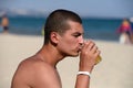 Young handsome sporty man drinking beer at the beach in summertime - relaxing, summer, thirsty concept. Resort relaxation. Sea in