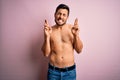 Young handsome strong man with beard shirtless standing over isolated pink background gesturing finger crossed smiling with hope Royalty Free Stock Photo