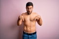 Young handsome strong man with beard shirtless standing over isolated pink background Pointing down with fingers showing Royalty Free Stock Photo