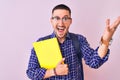 Young handsome student man holding a book over isolated background very happy and excited, winner expression celebrating victory Royalty Free Stock Photo