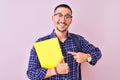 Young handsome student man holding a book over isolated background very happy pointing with hand and finger Royalty Free Stock Photo