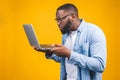 Young surprised african american man standing and using laptop computer isolated over yellow background Royalty Free Stock Photo