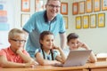 Young handsome teacher with group of clever children working with laptop during a lesson Royalty Free Stock Photo