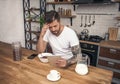 Young handsome thoughtful man is having his breakfast cereals with milk at the kitchen and reading morning news on the tablet Royalty Free Stock Photo