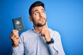 Young handsome tourist man holding australia australian passport id over blue background serious face thinking about question,