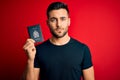 Young handsome tourist man holding canada canadian passport id over red background with a confident expression on smart face