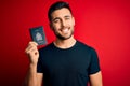 Young handsome tourist man holding canada canadian passport id over red background with a happy face standing and smiling with a