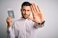 Young handsome tourist man holding united states passport id with dollars with open hand doing stop sign with serious and Royalty Free Stock Photo