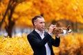 Young handsome trumpeter playing his musical instrument golden trumpet in autumn park