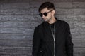 Young handsome urban man model with a stylish hairstyle with a beard in vintage dark sunglasses in a fashionable black jacket Royalty Free Stock Photo