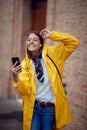 A young handsome woman in a yellow raincoat is enjoying music while walking the city on a rainy day. Walk, rain, city Royalty Free Stock Photo