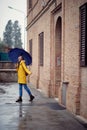 A young handsome woman in a yellow raincoat and with umbrella is happy about rain while walking the city. Walk, rain, city Royalty Free Stock Photo