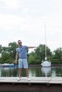 Young handsome yachtsman in sun glasses walking at river pier and welcomes friends. Handsome businessman invites to his boat.