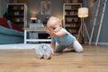 Young happy adorable baby girl or boy sitting on the floor of apartment playing with his or her favorite toy. Cute child crawling Royalty Free Stock Photo