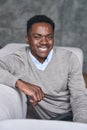 Young happy adult black man sitting on sofa at home looking at camera. Royalty Free Stock Photo