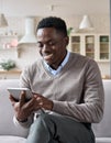 Young happy adult black man sitting on sofa at home using tablet device. Royalty Free Stock Photo