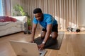 Young happy black African america male working out at home doing an online class using his laptop in his living room