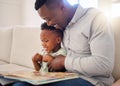 Young happy African american father reading a book with his son sitting on the couch at home. Little boy enjoying a Royalty Free Stock Photo