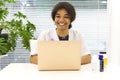 Young happy African-American female doctor sitting at workplace looking to the camera Royalty Free Stock Photo