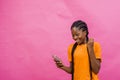 Young happy African-American female holding a cellular phone isolated on light pink background