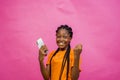 Young happy African-American female holding a cellular phone isolated on light pink background