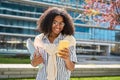 Young happy African American girl walking in city park using mobile phone. Royalty Free Stock Photo