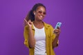 Young happy African American woman holding phone in hands and pointing finger up Royalty Free Stock Photo