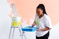 Young happy african american woman painting interior wall with paint roller in new house. A woman with roller applying Royalty Free Stock Photo