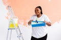 Young happy african american woman painting interior wall with paint roller in new house. A woman with roller applying Royalty Free Stock Photo