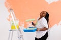 Young happy african american woman painting interior wall with paint roller in new house. A woman with roller applying Royalty Free Stock Photo