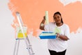 Young happy african american woman painting interior wall with paint roller in new house. A woman with roller applying Royalty Free Stock Photo