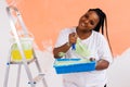 Young happy african american woman painting interior wall with paint roller in new house. A woman with roller applying Royalty Free Stock Photo