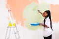 Young happy african american woman painting interior wall with paint roller in new house. A woman with roller applying Royalty Free Stock Photo