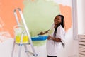 Young happy african american woman painting interior wall with paint roller in new house. A woman with roller applying Royalty Free Stock Photo