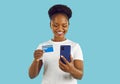 Young happy African American woman uses credit card to shop on mobile phone, stands in studio Royalty Free Stock Photo