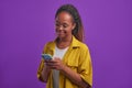 Young happy African American woman uses phone stands in lilac studio Royalty Free Stock Photo