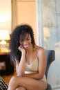 Young happy black girl sitting in room and wearing beige lingerie. Royalty Free Stock Photo