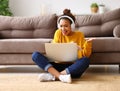 Happy african american teen girl in headphones sitting on floor and  having video call while working or studying online on sofa at Royalty Free Stock Photo