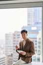 Young happy Asian business man holding tablet sitting in office. Vertical Royalty Free Stock Photo