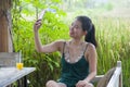 Happy Asian Chinese woman on her 20s or 30s smiling having fun taking selfie pic with mobile phone at rice field cafe having orang Royalty Free Stock Photo