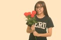 Young happy Asian nerd teenage girl smiling and holding red roses ready for Valentine's day Royalty Free Stock Photo