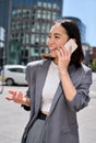 Young happy Asian business woman wears suit talking on the phone on city street. Royalty Free Stock Photo