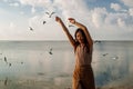 Happy asian woman with hands in the air walks on the seaside in autumn. Seagulls flying on the beach. Royalty Free Stock Photo