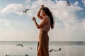 Happy asian woman with hands in the air walks on the seaside in autumn. Seagulls flying on the beach. Royalty Free Stock Photo